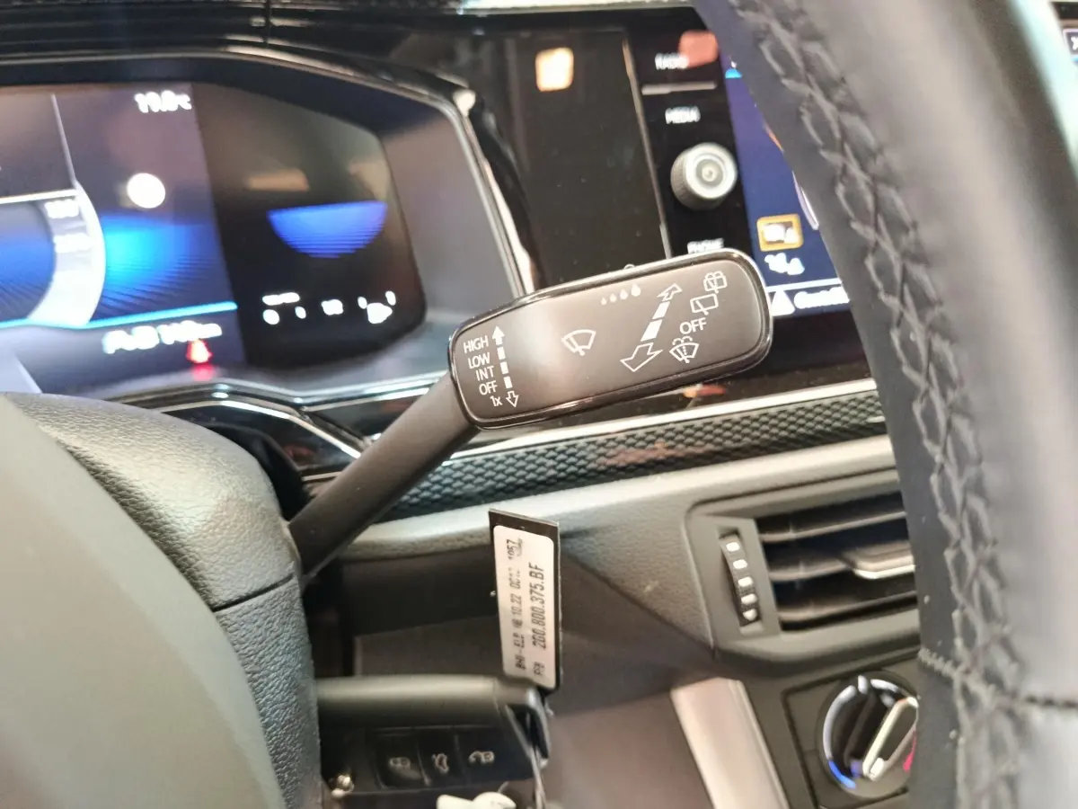 Gros plan sur la manette d’essuie-glace à gauche du volant cuir d’une Volkswagen Polo gris clair, tableau de bord numérique en arrière-plan.