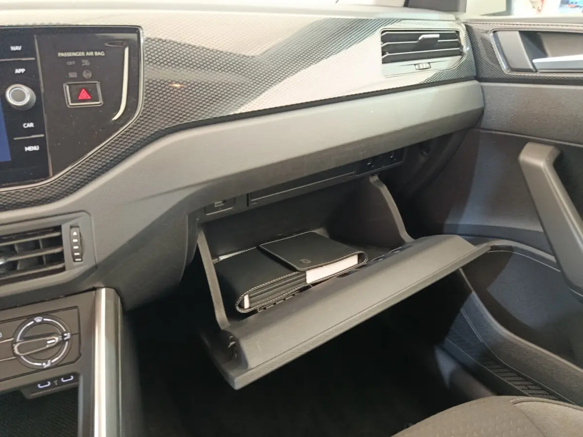 Vue intérieure côté passager de la Volkswagen Polo 2023 gris clair, boîte à gants ouverte avec documents visibles.
