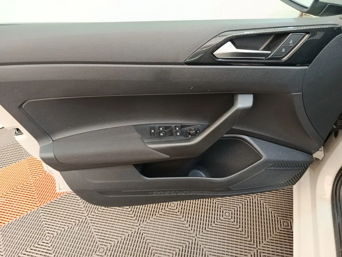 Vue latérale du panneau de porte avant gauche noir d'une Volkswagen Polo 2023, avec commandes électriques et poignée intégrée.