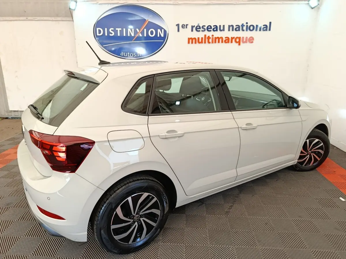 Vue 3/4 arrière droite d'une Volkswagen Polo gris clair avec jantes alliage noires et rouges en intérieur showroom.