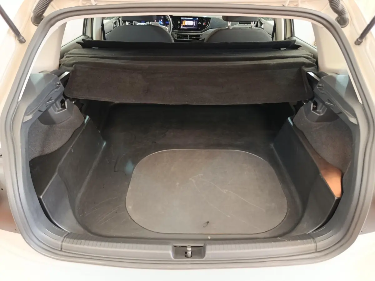 Coffre ouvert vu de l'arrière d'une Volkswagen Polo gris clair, avec cache-bagages déployé et intérieur noir.