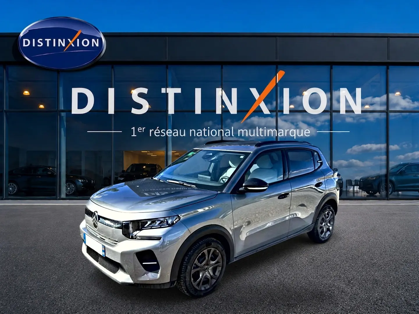 Vue 3/4 avant d'une Citroën C3 gris mercure garée devant une vitrine avec logo Distinxion.