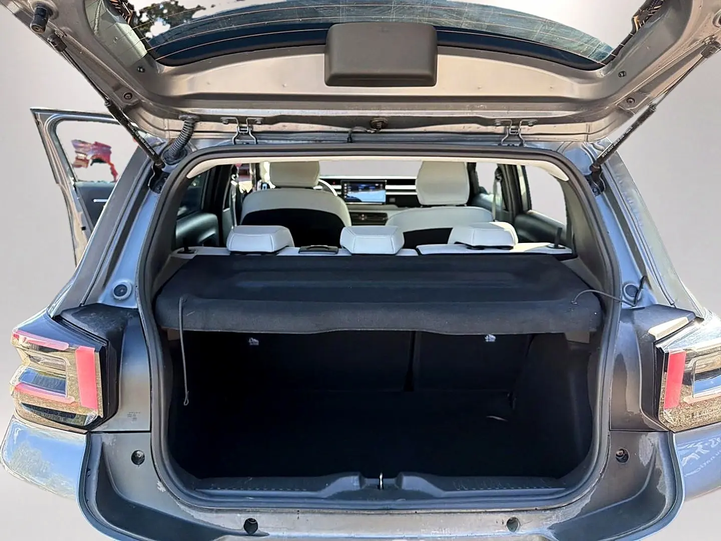 Vue arrière ouverte du coffre d'une Citroën C3 gris mercure, avec banquette arrière blanche et cache-bagages noir.