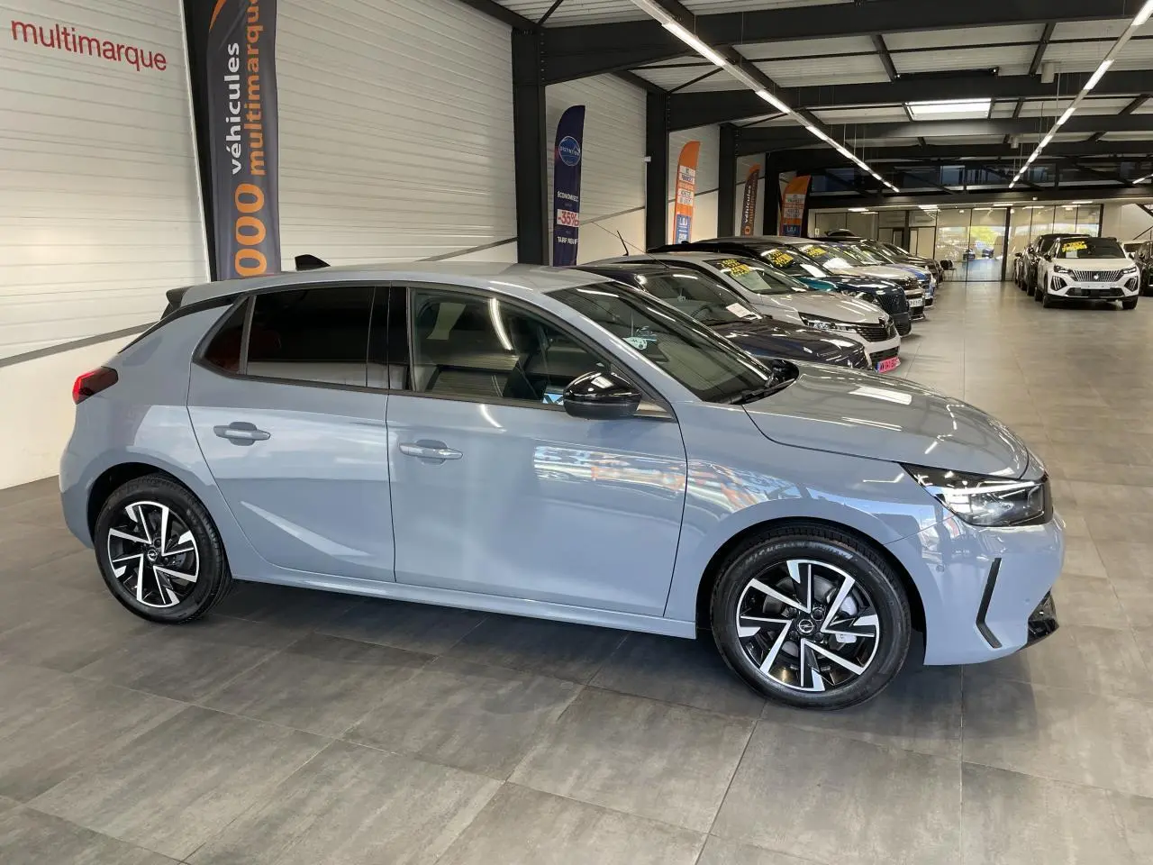 Opel Corsa gris clair vue de profil côté droit, avec jantes alliage noires et vitres arrière surteintées.