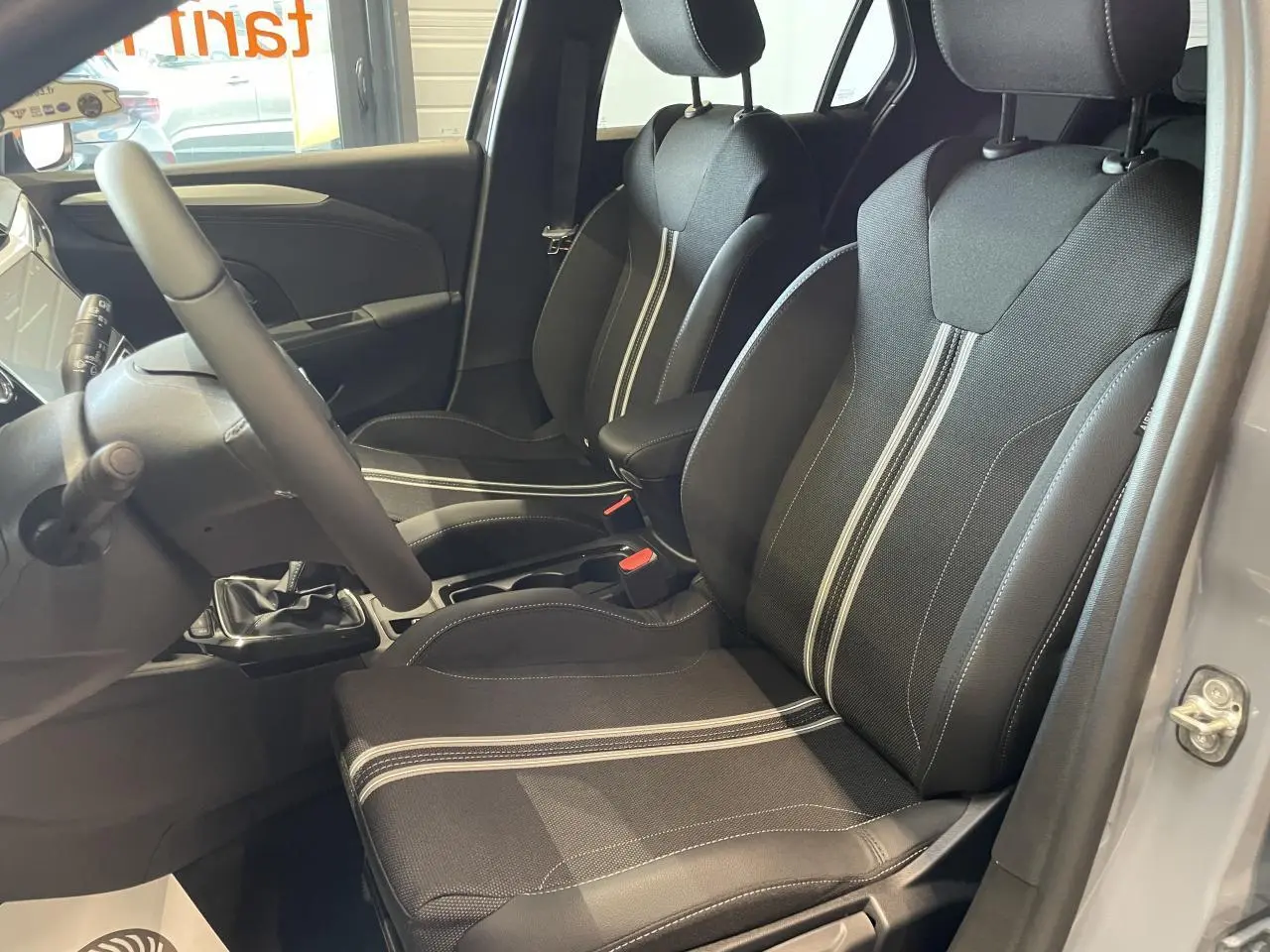 Intérieur avant droit d’Opel Corsa gris, sièges sport noirs avec bandes blanches et volant cuir synthétique.