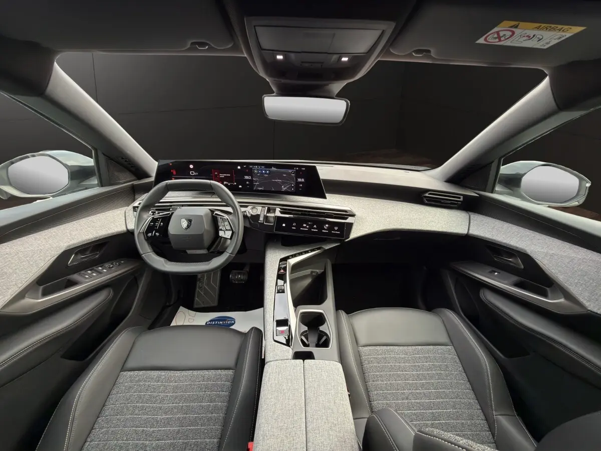 Vue intérieure avant du Peugeot 3008 2025 hybride, tableau de bord gris clair et sièges cuir noir avec tissu gris.