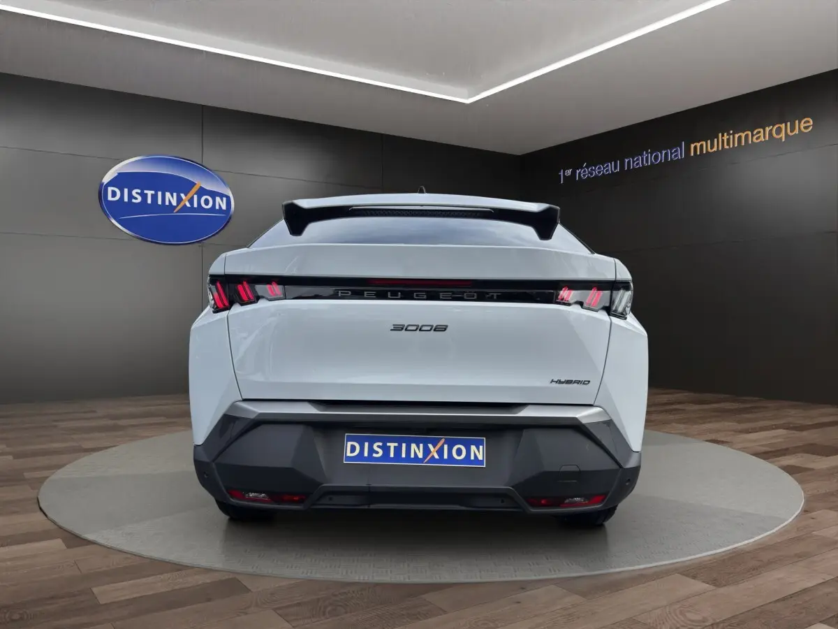 Vue arrière d’un Peugeot 3008 blanc hybride 2025 avec feux arrière LED et logo distinctif sur fond showroom.