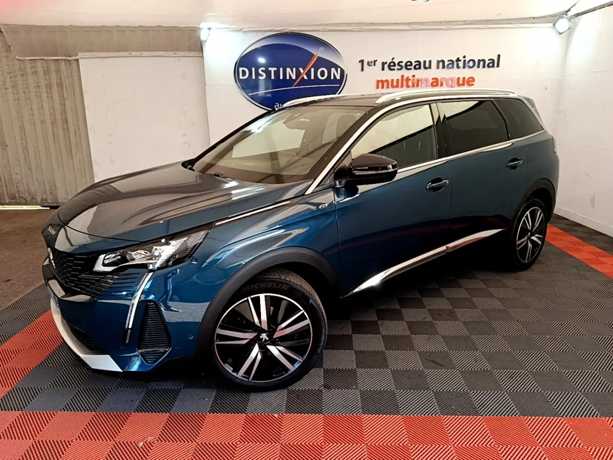 Peugeot 5008 bleu en 3/4 avant droit, jantes alliage noires et chrome, stationné en intérieur showroom