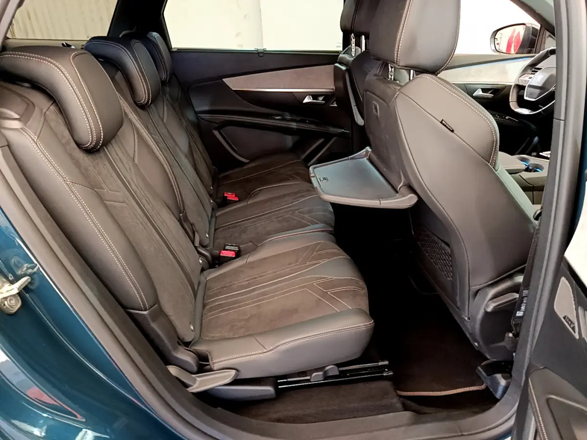 Vue côté gauche de l'intérieur arrière du Peugeot 5008 bleu, sièges en cuir marron avec tablette rabattable intégrée.