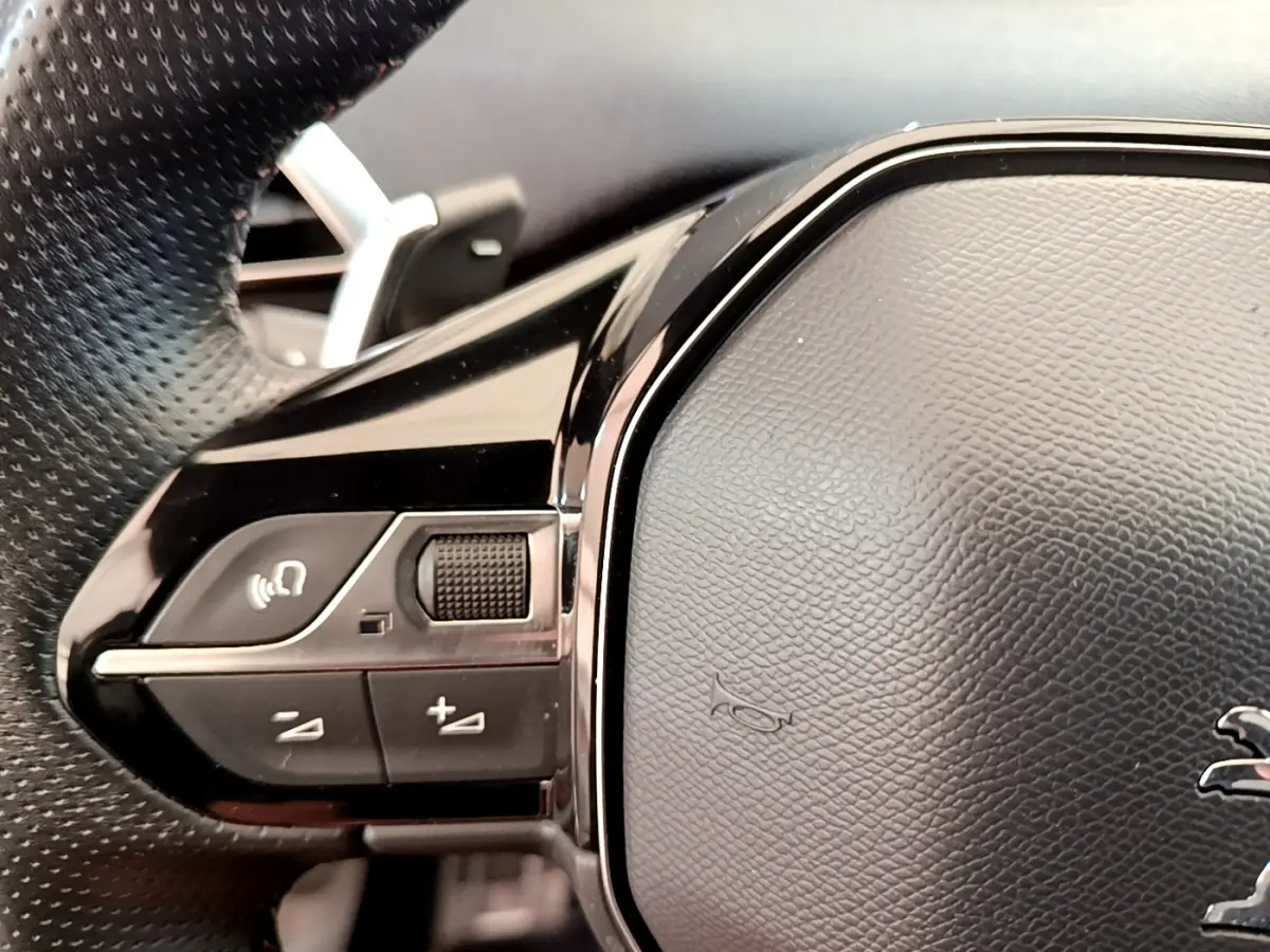Gros plan sur les commandes gauche du volant cuir noir du Peugeot 5008 bleu, avec logo lion visible.
