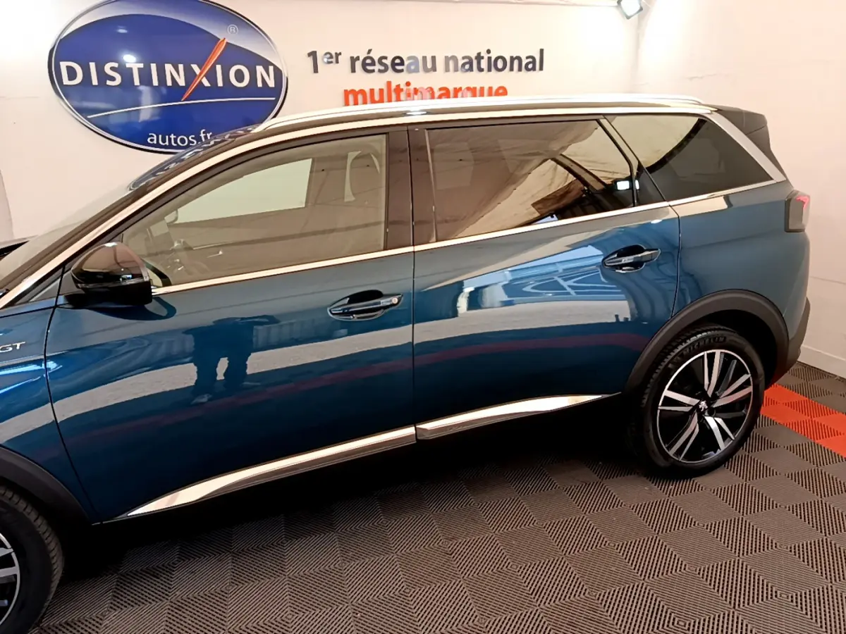 Profil côté gauche du Peugeot 5008 bleu 2021 GT Pack avec jantes alliage et vitres teintées en intérieur showroom.