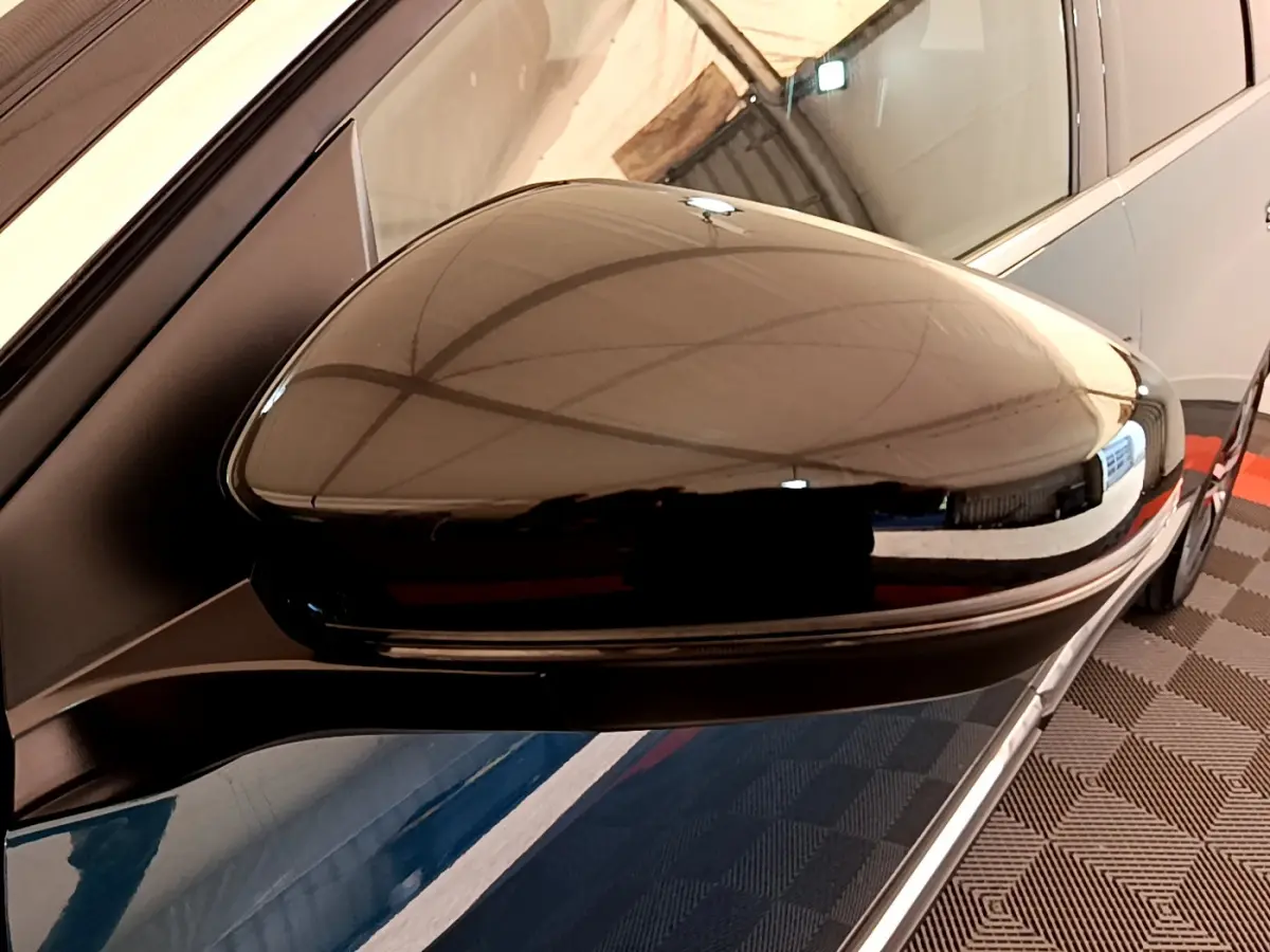 Rétroviseur côté gauche noir brillant du Peugeot 5008 bleu, vue rapprochée avec reflet de l'environnement intérieur.