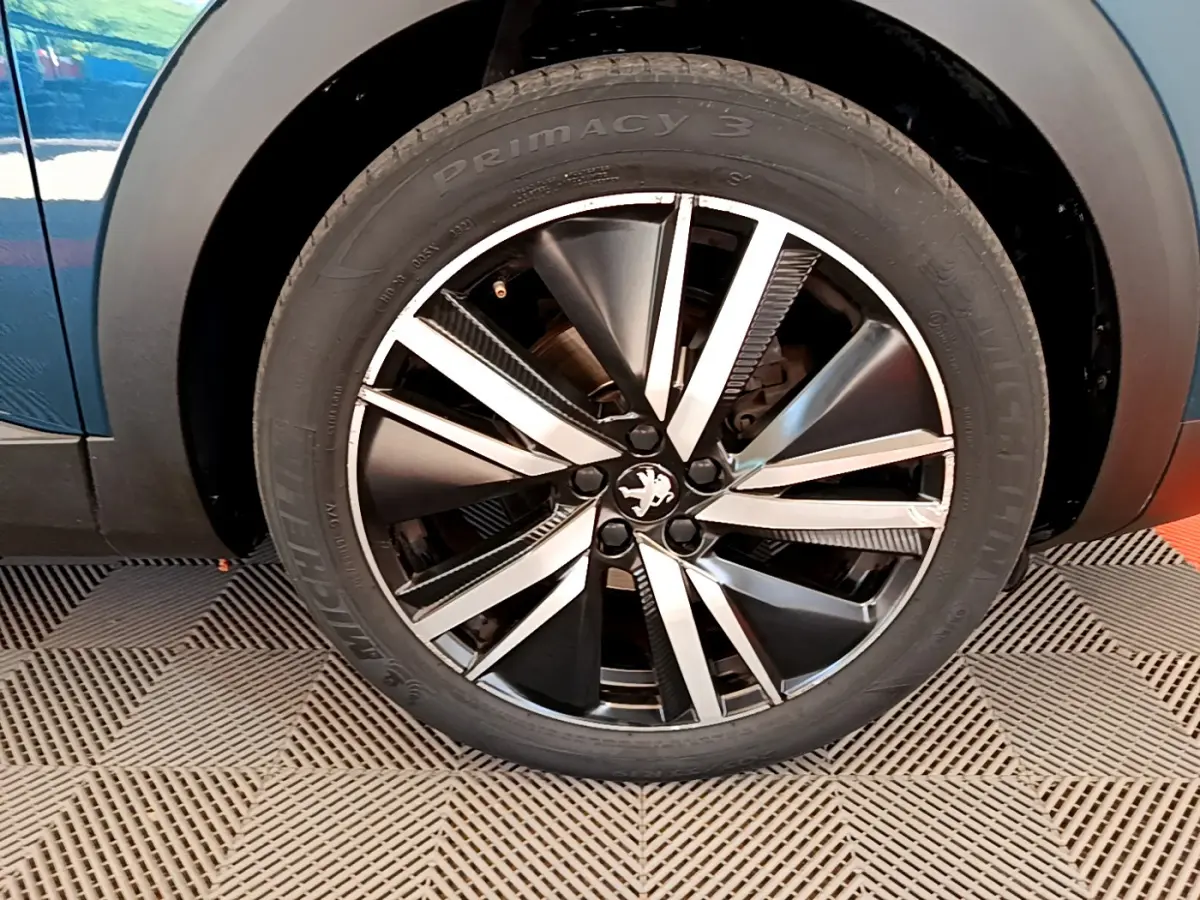 Gros plan sur la roue avant droite du Peugeot 5008 bleu, mettant en valeur la jante alliage au design moderne.