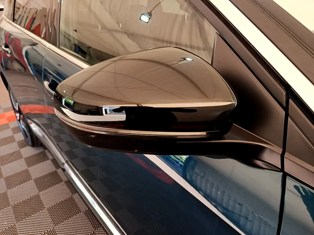 Rétroviseur côté gauche noir brillant du Peugeot 5008 bleu, avec carrosserie et poignée de porte visibles en arrière-plan.