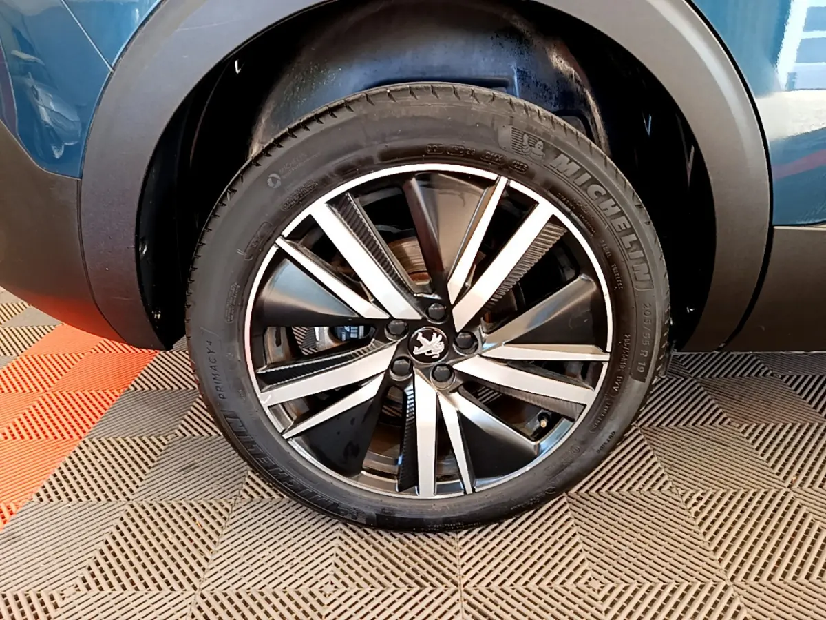 Gros plan sur la roue avant droite du Peugeot 5008 bleu, mettant en valeur la jante alliage bicolore et le pneu Michelin.