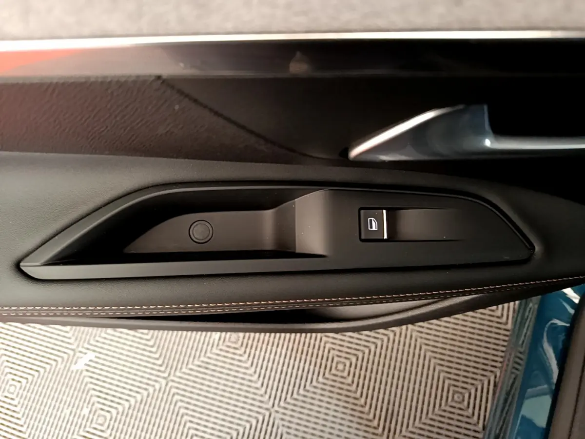 Poignée intérieure côté gauche de la porte d'un Peugeot 5008 bleu, avec bouton de verrouillage et surpiqûres marron.
