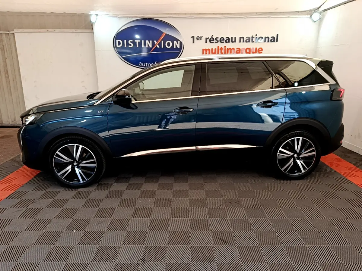 Profil côté gauche d'un Peugeot 5008 GT Pack bleu avec toit blanc et jantes alliage stylées en intérieur showroom.