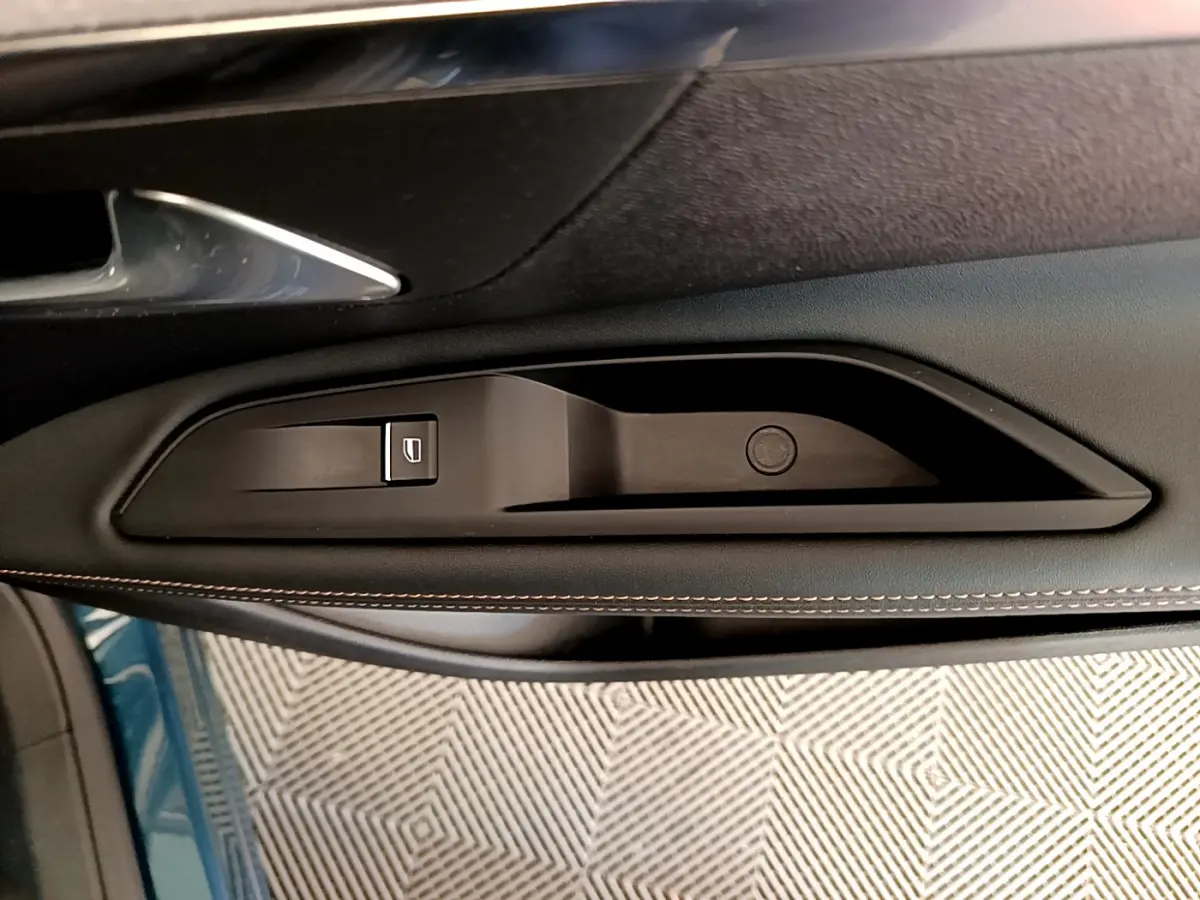 Poignée intérieure côté gauche de la porte d’un Peugeot 5008 bleu, avec bouton de commande de vitre électrique.