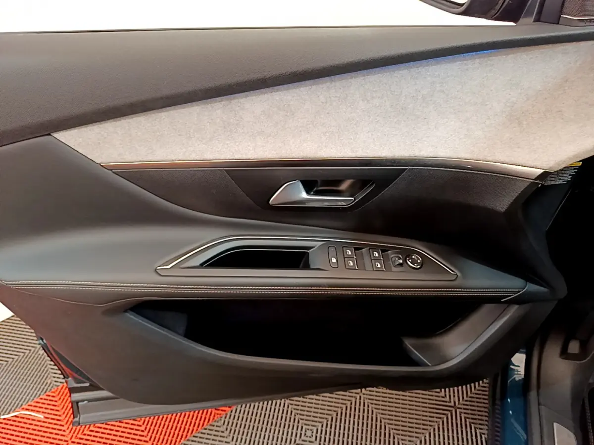 Gros plan sur la porte côté gauche du Peugeot 5008 bleu, montrant les commandes des vitres et la poignée intérieure.