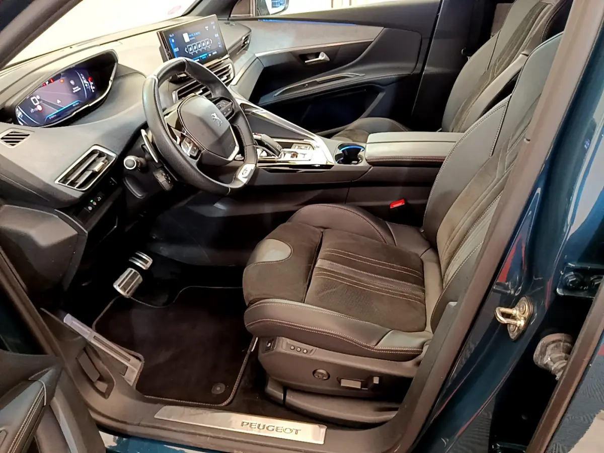 Vue intérieure côté conducteur du Peugeot 5008 bleu, mettant en valeur le tableau de bord digital et les sièges en cuir noir.