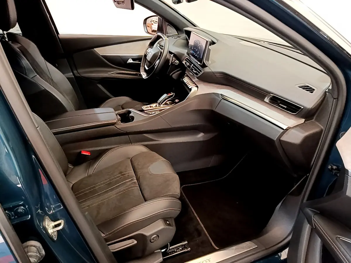 Vue intérieure côté conducteur du Peugeot 5008 bleu 2021, avec tableau de bord moderne et sièges en cuir noir.