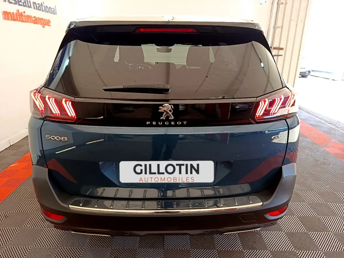 Vue arrière d'un Peugeot 5008 bleu avec feux LED en forme de griffes et logo lion central sur hayon noir brillant.