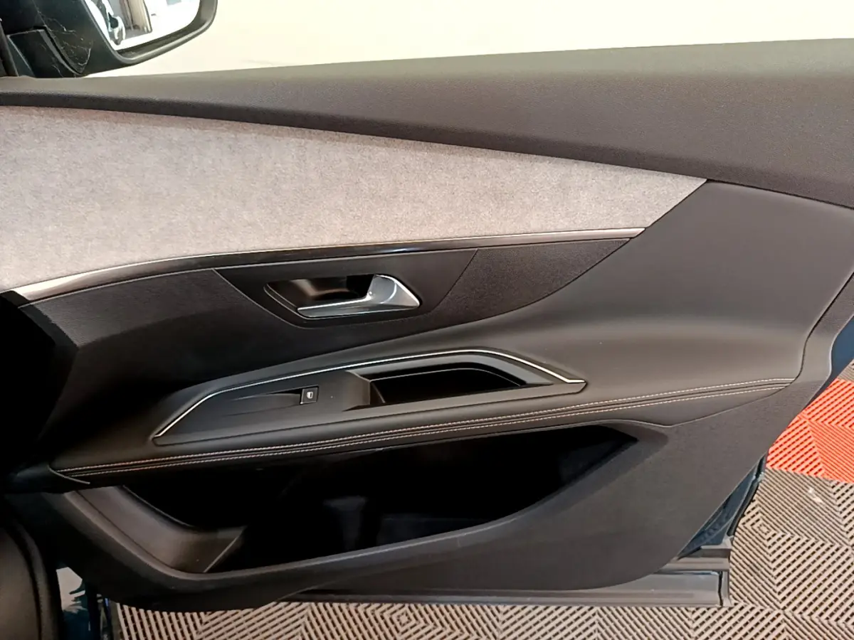 Gros plan sur la garniture de la porte côté droit du Peugeot 5008 bleu, avec insert tissu clair et surpiqûres blanches.