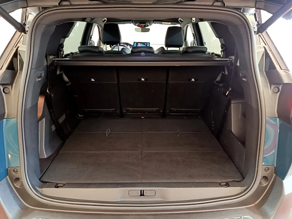 Coffre ouvert vu de l'arrière d'un Peugeot 5008 bleu 2021, sièges rabattus offrant un plancher plat spacieux.