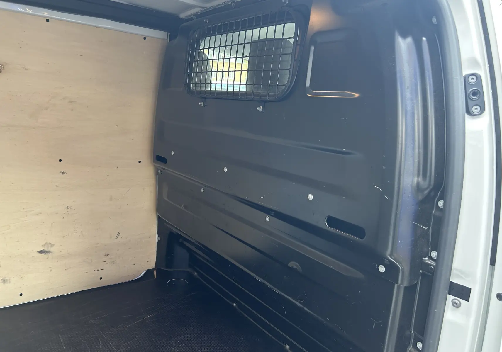 Vue intérieure du fourgon blanc Citroën Jumpy 2019, montrant la cloison métallique avec grille de séparation et le revêtement bois côté gauche.