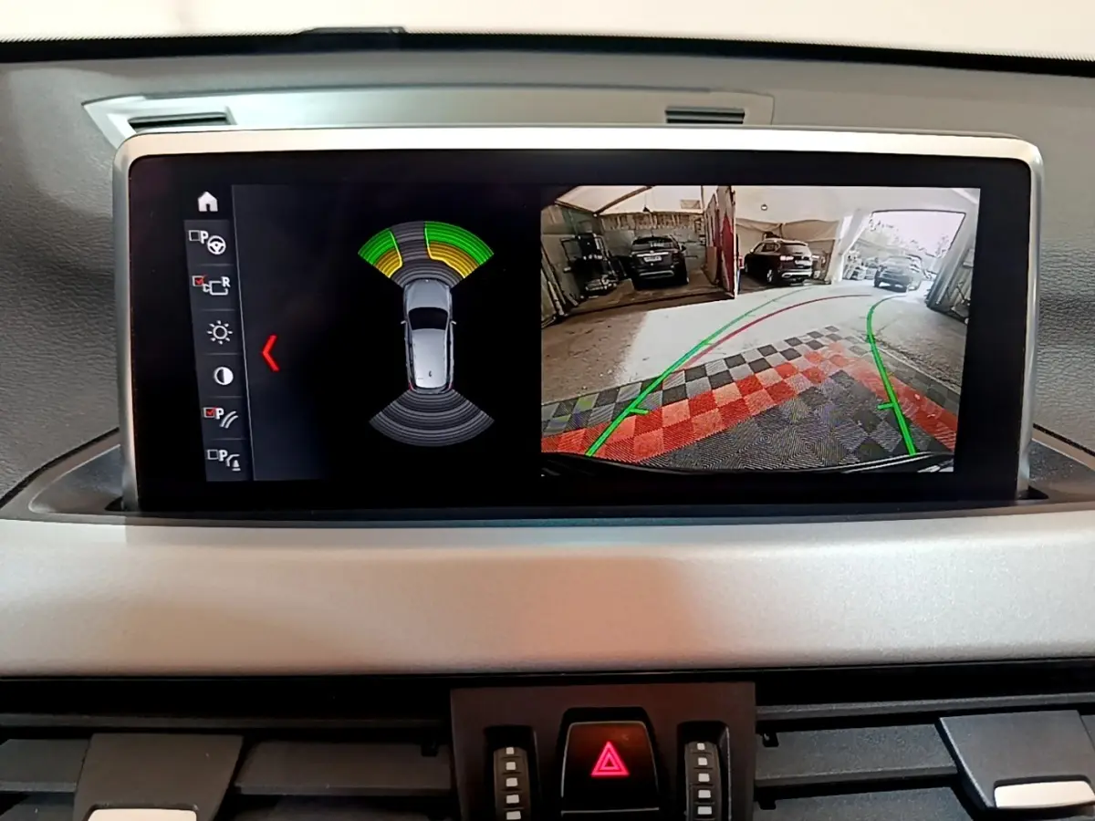 Écran tactile du tableau de bord BMW X1 noir 2020 affichant caméra de recul et capteurs de stationnement.