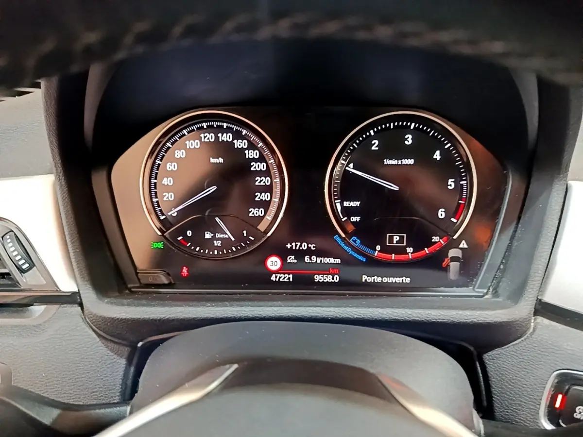 Tableau de bord numérique BMW X1 2020 sDrive16d noir, affichage vitesse, compte-tours et alertes porte ouverte.