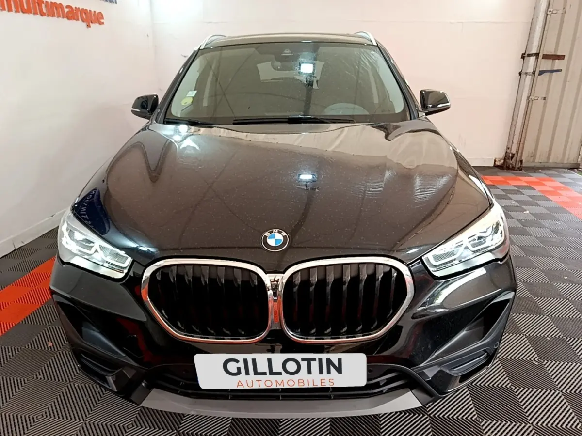 Vue frontale d'un BMW X1 noir 2020 avec calandre double haricot et phares LED allumés dans un showroom.