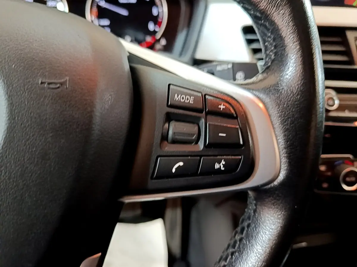 Gros plan sur les commandes du volant en cuir noir d'une BMW X1 sDrive16d Business Design 2020.