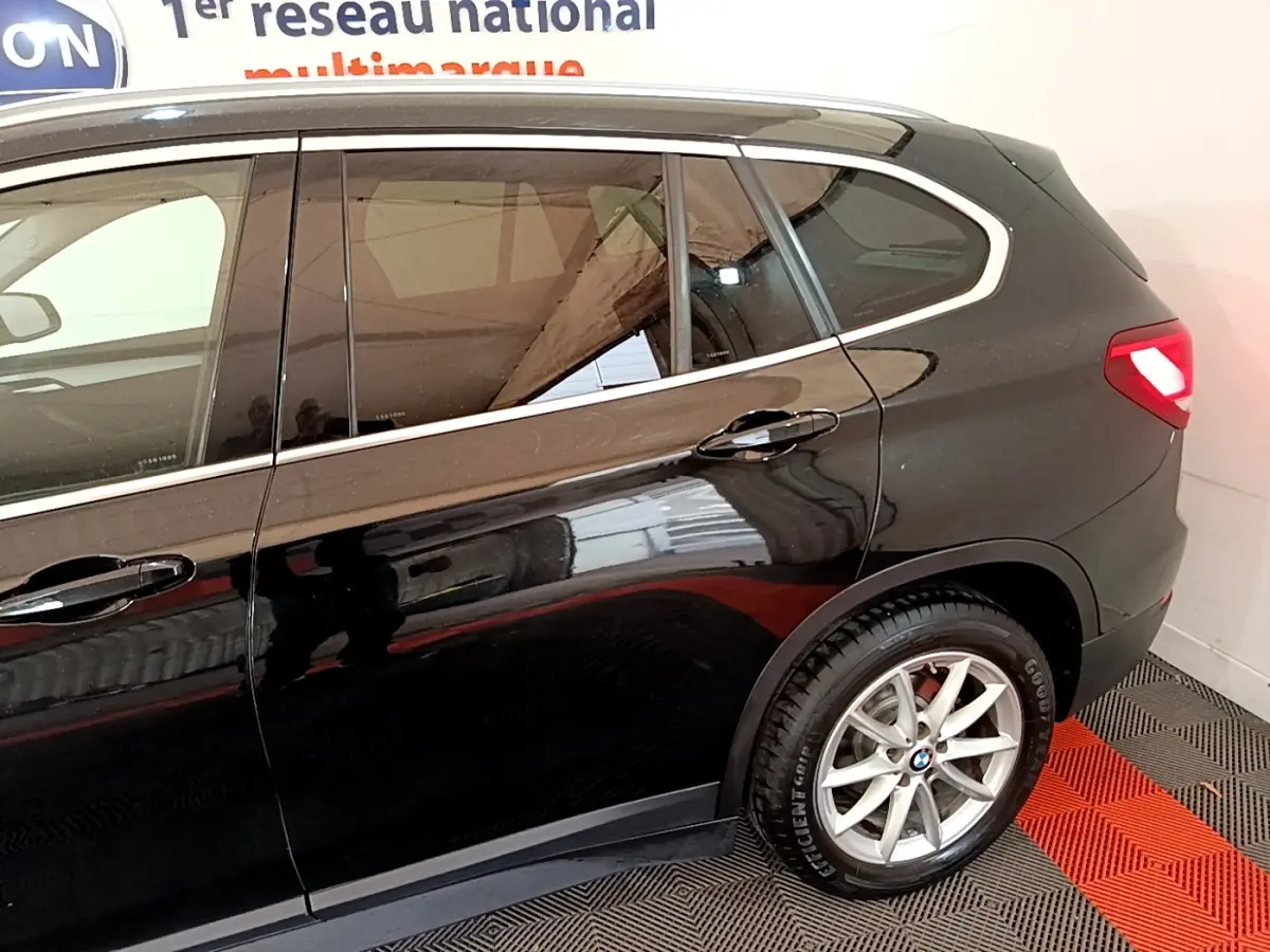 Vue latérale côté droit d'un BMW X1 noir 2020 avec jante alliage et feux arrière allumés.