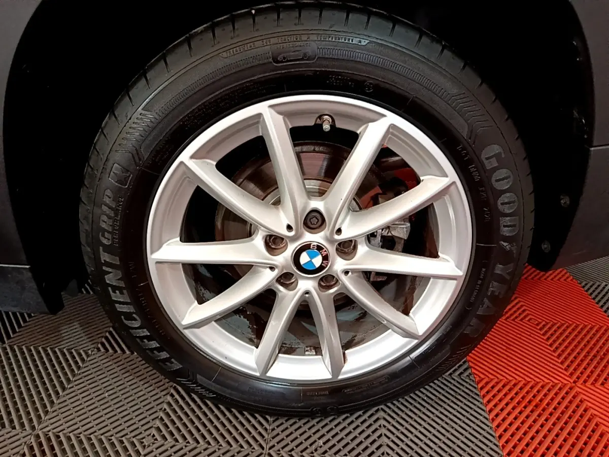 Gros plan sur la jante alliage argentée avec logo BMW centrale, montée sur pneu Goodyear, sur BMW X1 noir.