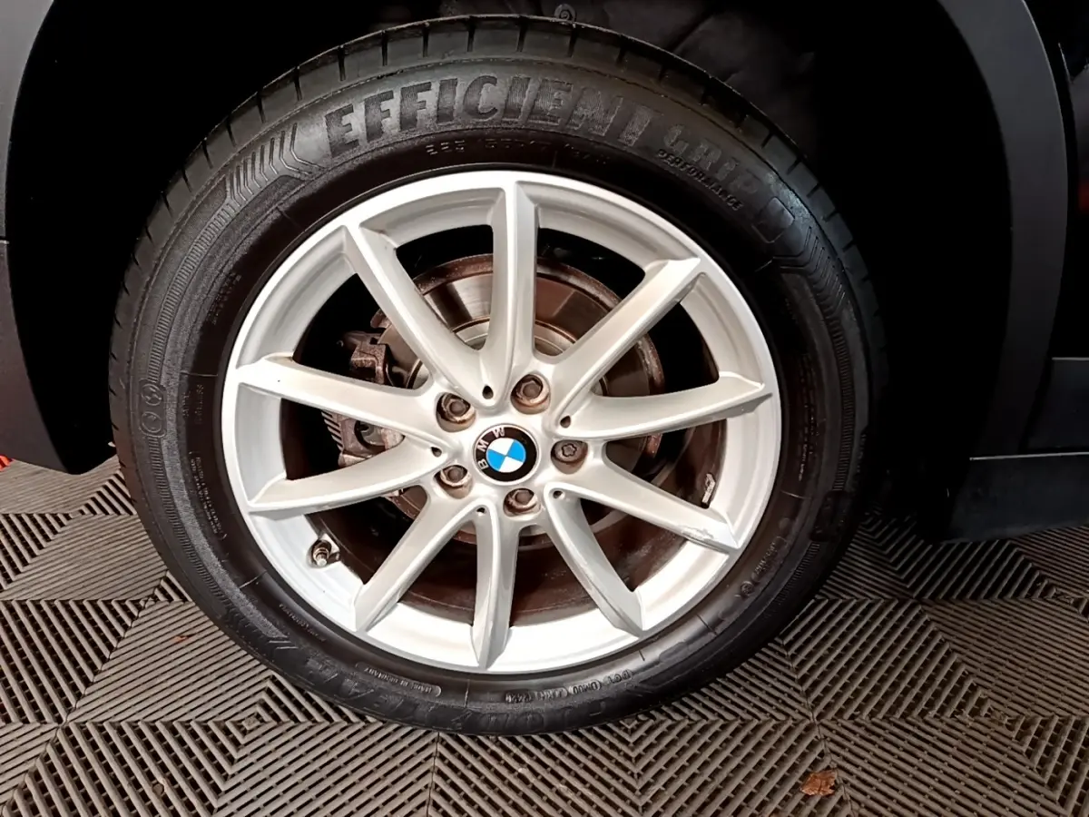 Gros plan sur la roue avant droite noire d'un BMW X1 2020 avec jante argentée à 7 branches fines