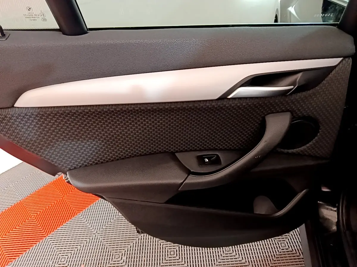Gros plan sur la porte intérieure côté gauche d'un BMW X1 noir, avec poignée et bouton de verrouillage visibles.