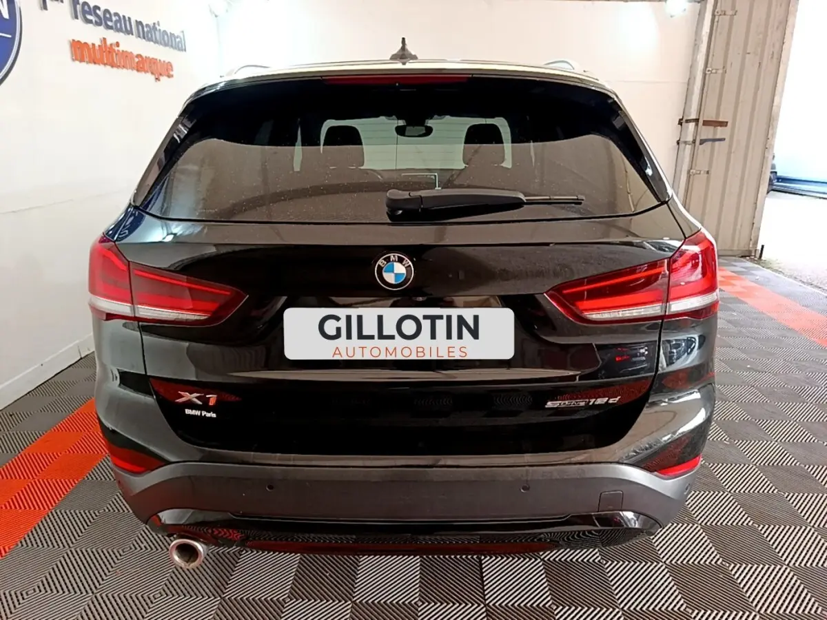 Vue arrière d'un BMW X1 noir sDrive16d avec feux LED et sortie d'échappement visible en intérieur showroom.