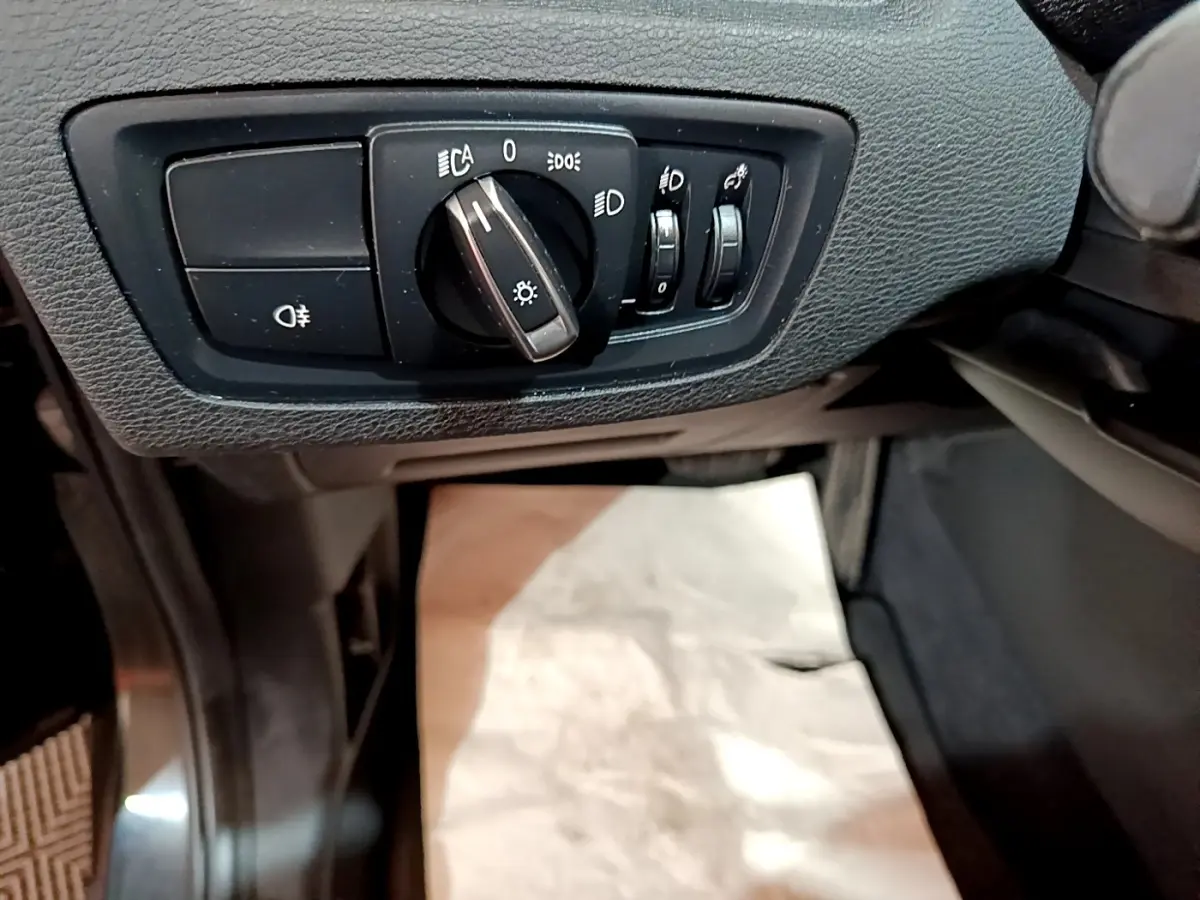 Gros plan sur les commandes d'éclairage côté gauche du tableau de bord noir du BMW X1 sDrive16d Business Design 2020.