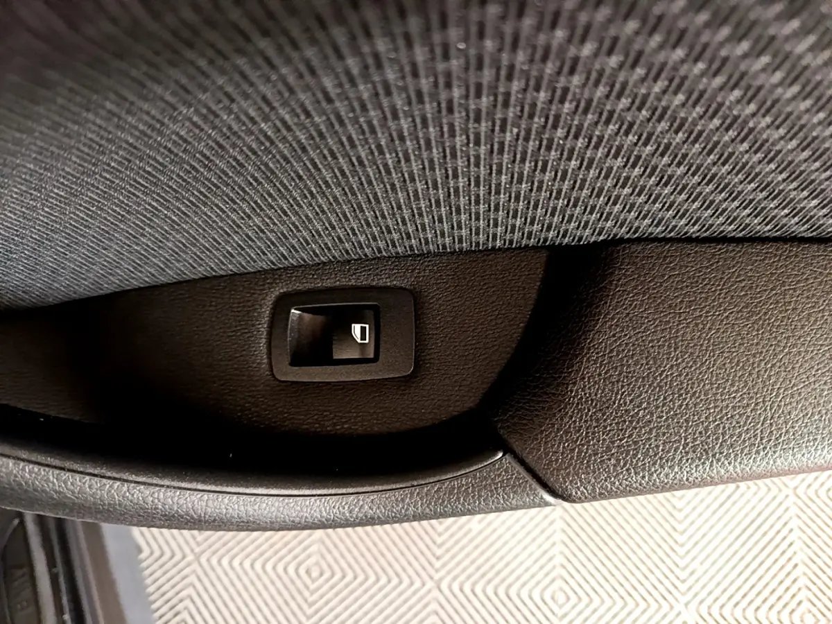 Gros plan sur le bouton de commande de lève-vitre noir, côté intérieur d'une BMW X1 sDrive16d Business Design 2020.