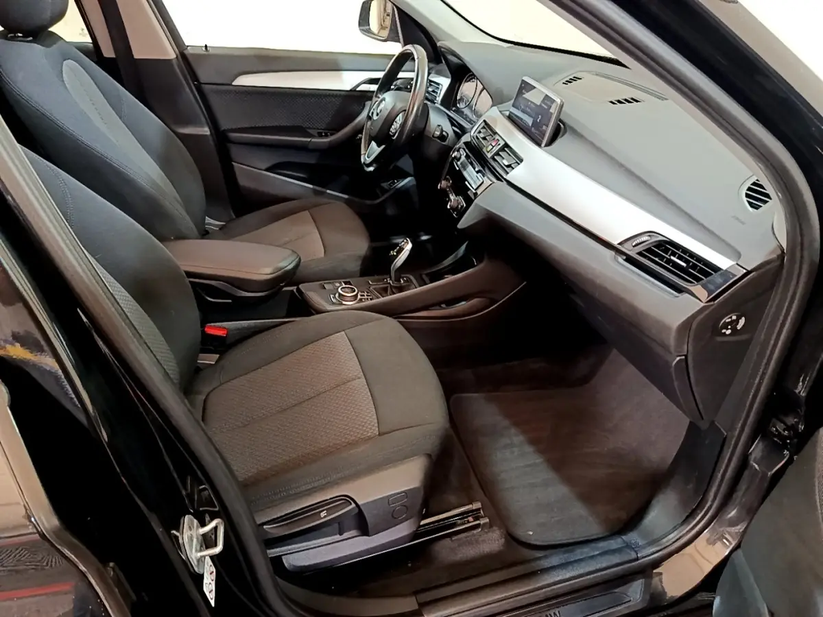 Intérieur avant droit d'une BMW X1 noire 2020, sièges tissu gris, tableau de bord avec écran tactile et console centrale.