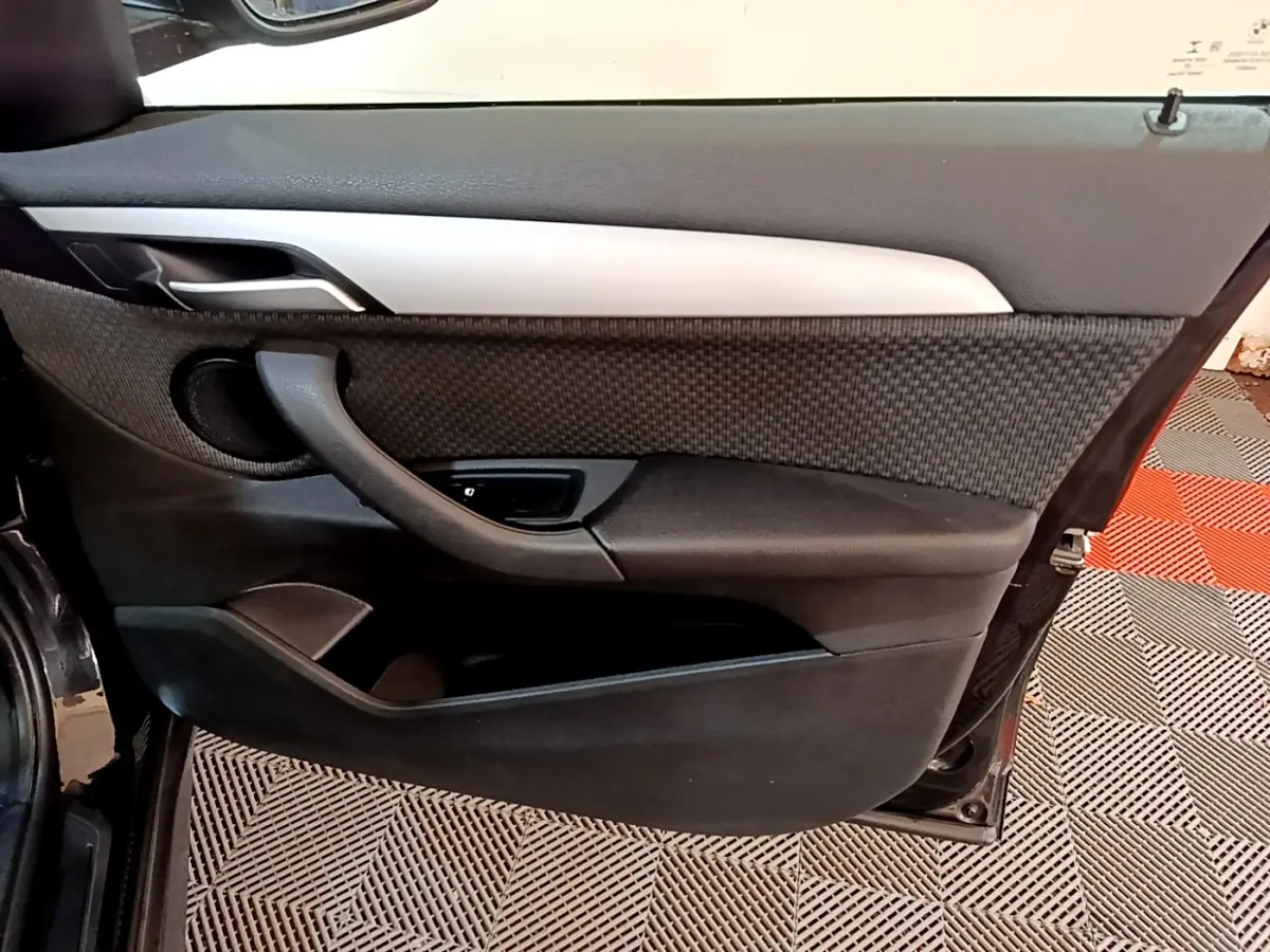 Porte intérieure côté gauche de BMW X1 noir 2020, avec habillage tissu et plastique noir, poignée intégrée et haut-parleur rond.