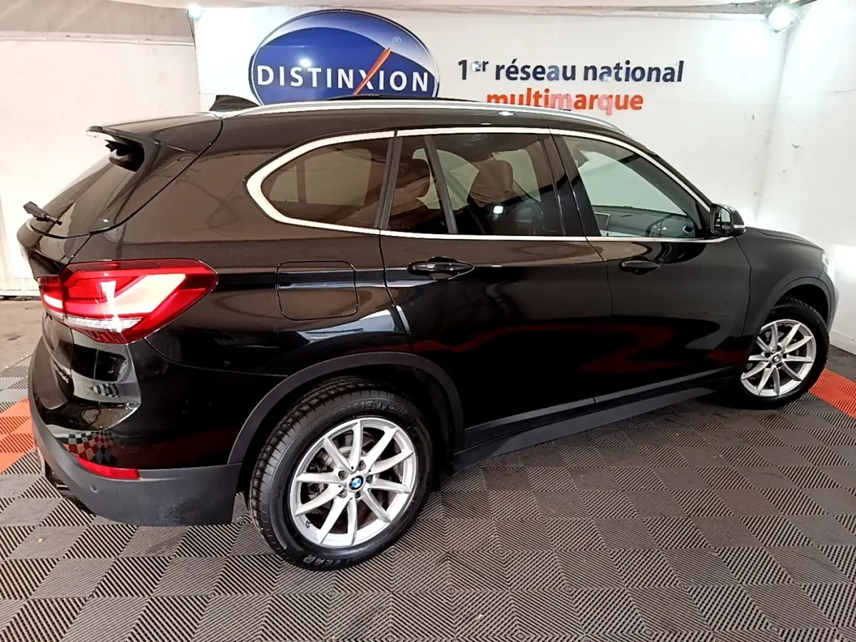 BMW X1 sDrive16d noir vue de profil côté gauche en intérieur avec jantes alliage et feux arrière LED allumés