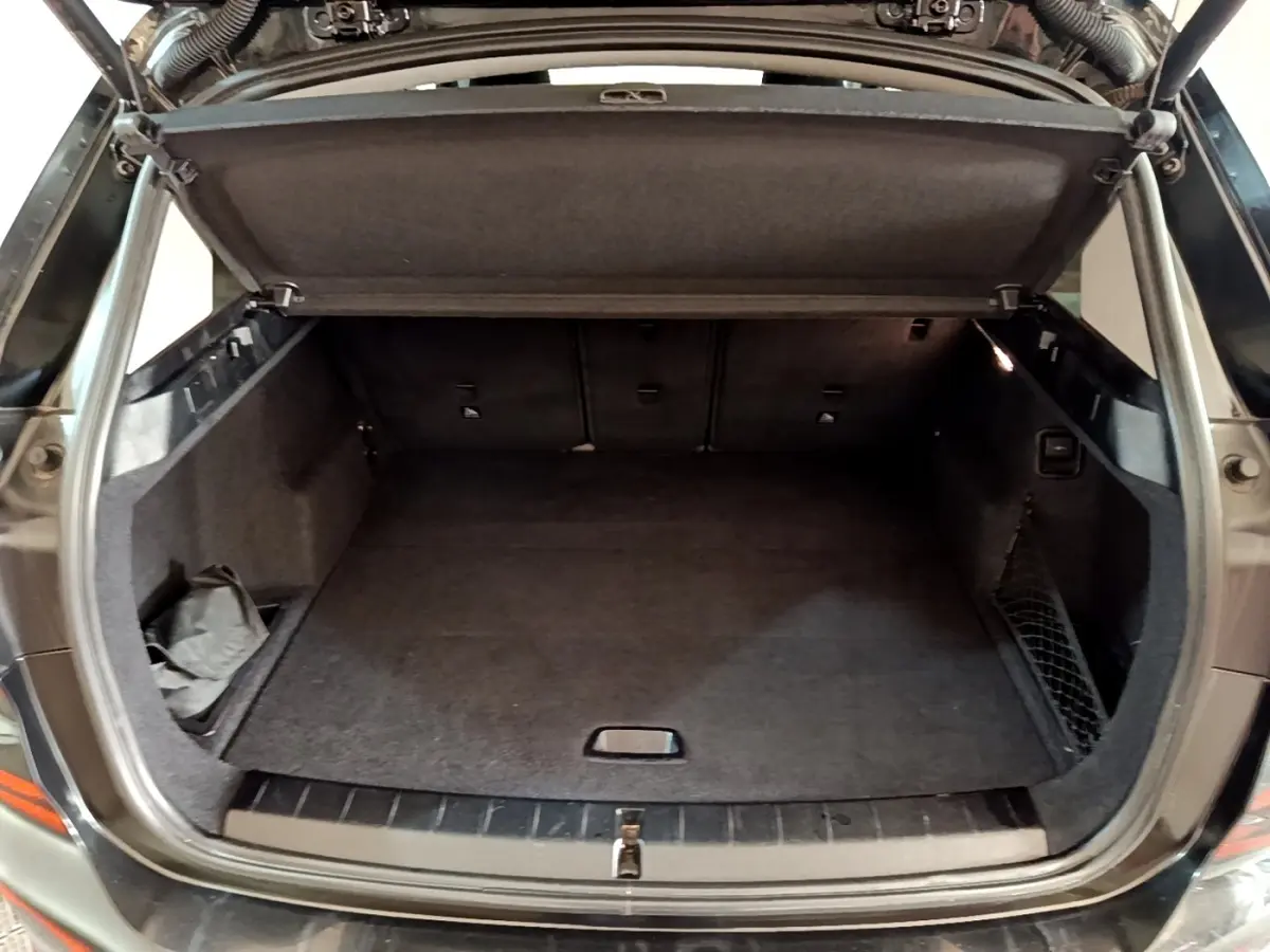 Coffre ouvert vu de l'arrière du BMW X1 noir, montrant un espace de chargement propre et bien agencé.