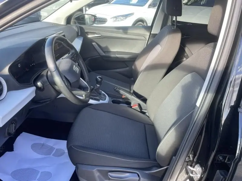 Vue intérieure côté conducteur du SEAT Arona noir 2023, montrant les sièges, volant et levier de vitesses manuel.