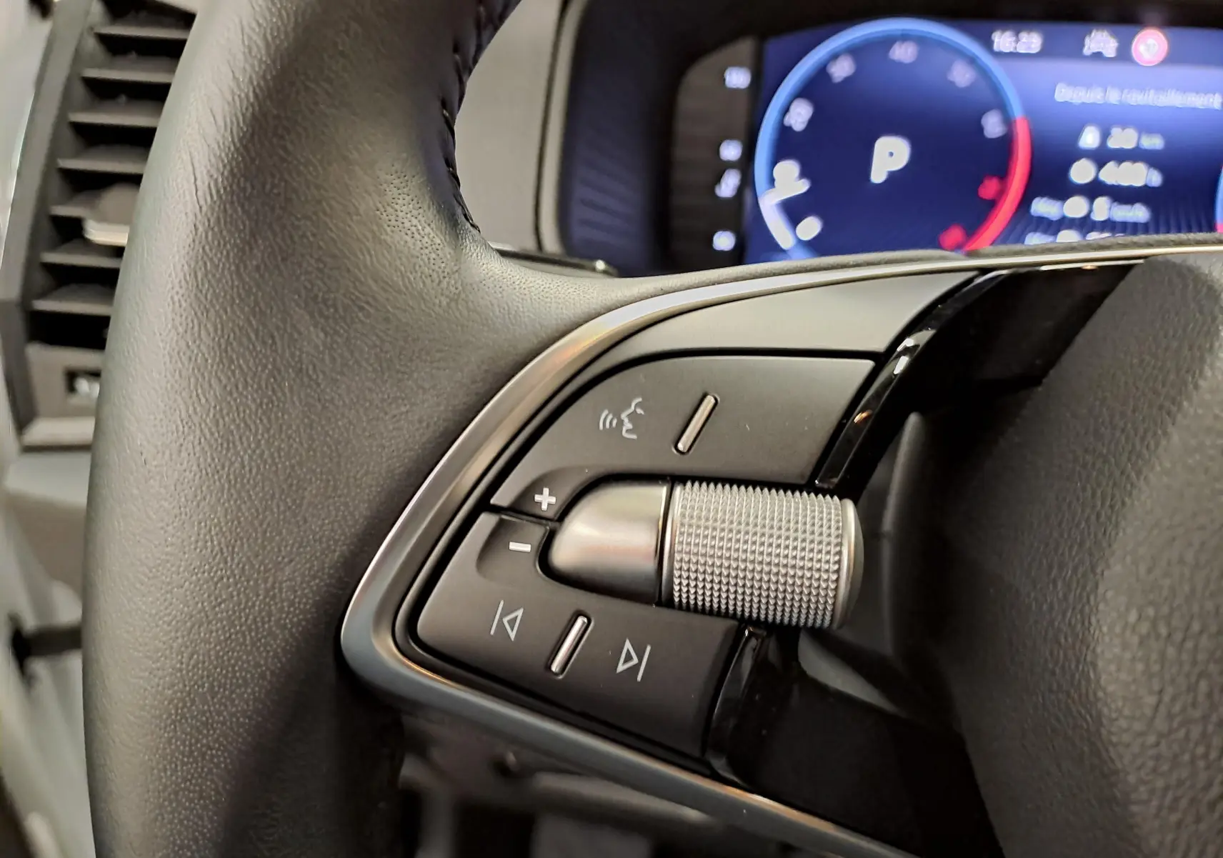 Gros plan sur les commandes gauche du volant du Skoda Karoq blanc lune 2025, avec molette crantée et tableau de bord numérique en arrière-plan.