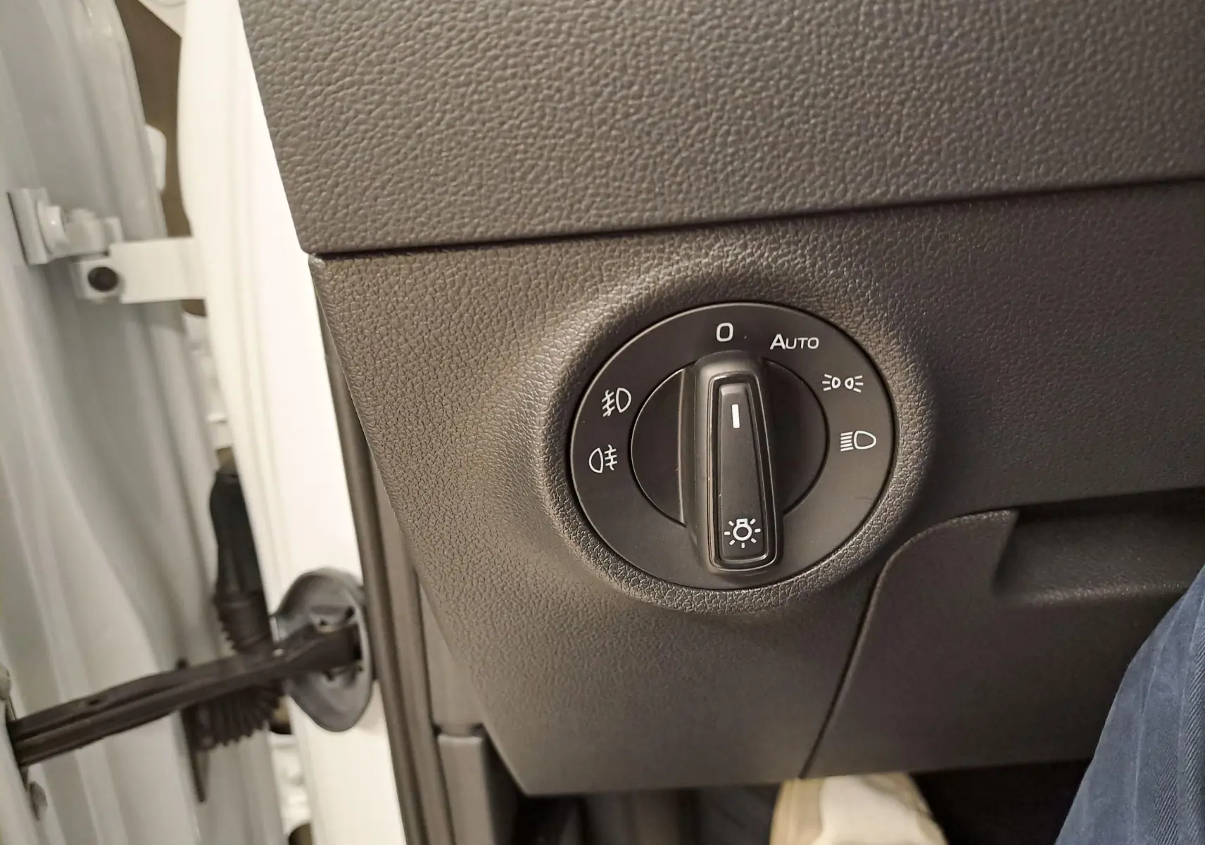Gros plan sur le bouton de réglage des phares dans l'habitacle d'un Skoda Karoq Blanc Lune 2025, côté conducteur.
