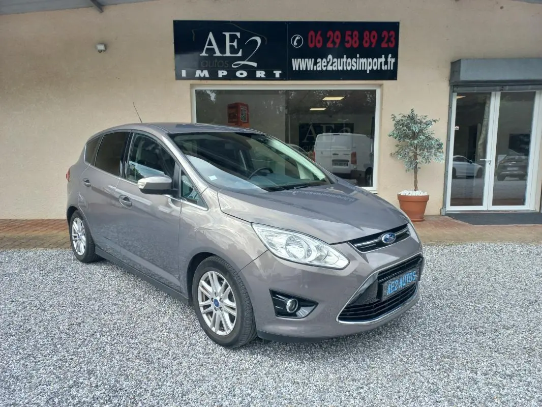 Ford C-MAX gris en 3/4 avant droit, avec calandre chromée et jantes alliage, stationné devant un commerce.