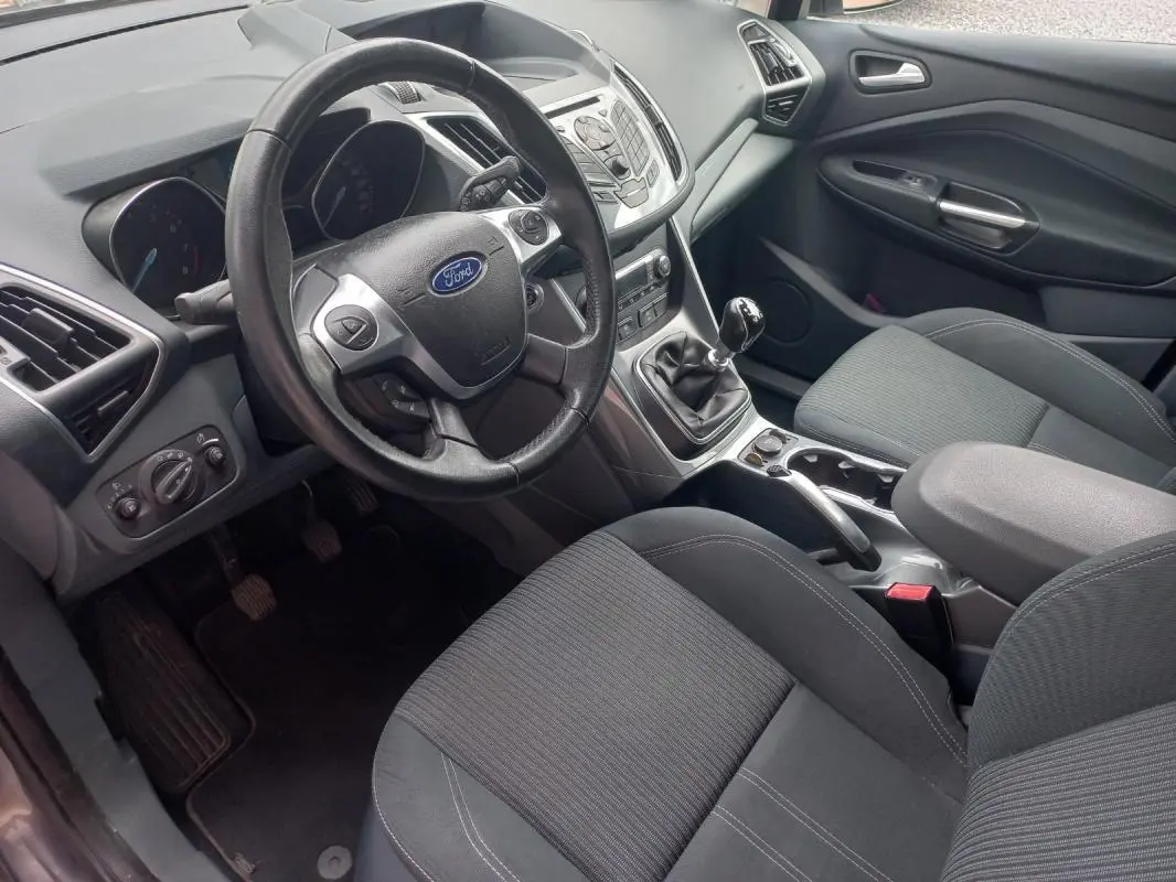 Vue intérieure côté conducteur du Ford C-MAX gris 2015, montrant le volant, la boîte manuelle et les sièges tissu noirs.