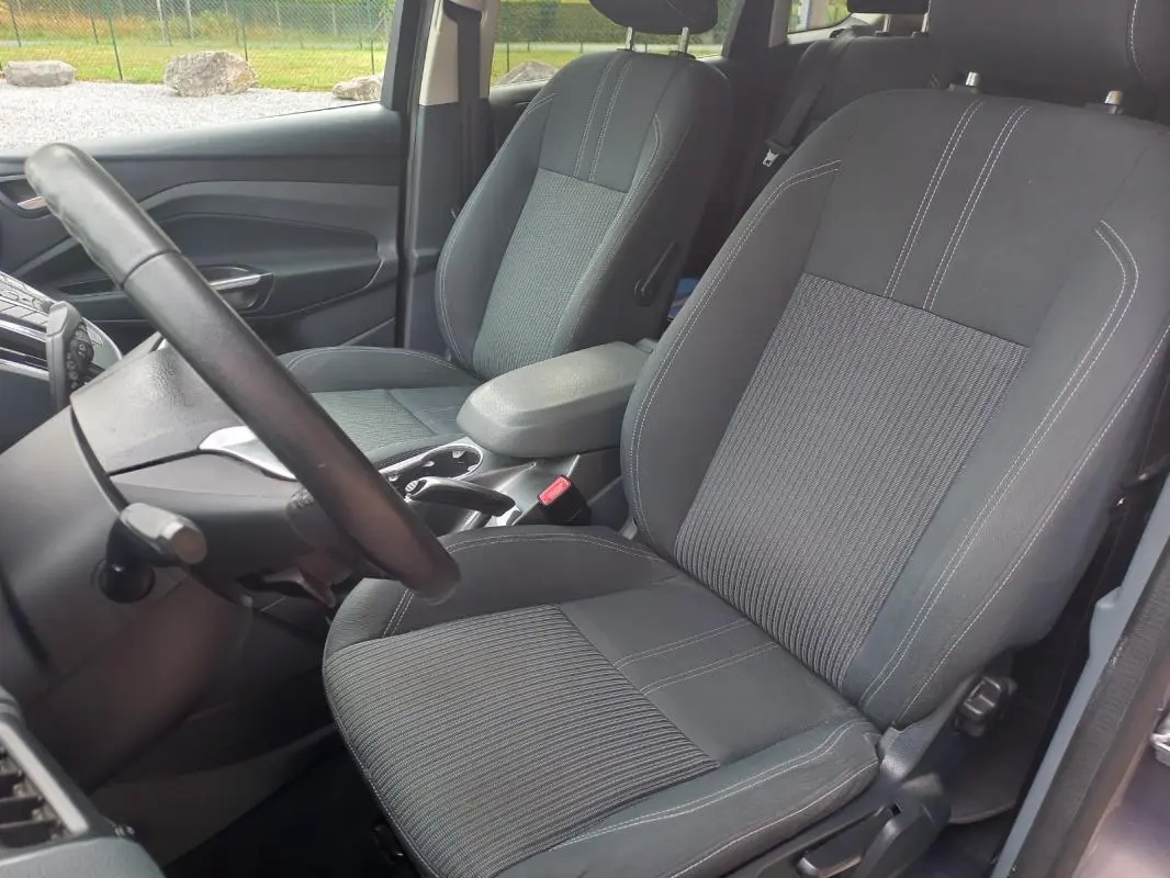 Vue intérieure côté conducteur du Ford C-MAX gris 2015, montrant les sièges avant en tissu avec coutures contrastées.